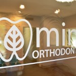 Photo of Mint Orthodontics logo on window looking into Waiting Room