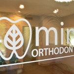Photo of Mint Orthodontics logo on window looking into Waiting Room