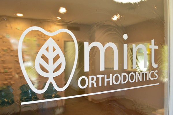 Photo of Mint Orthodontics logo on window looking into Waiting Room